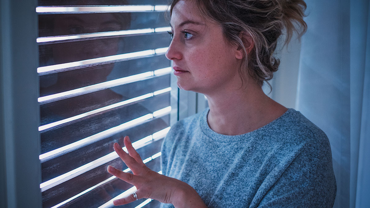 mujer mirando por la ventana con miedo a salir