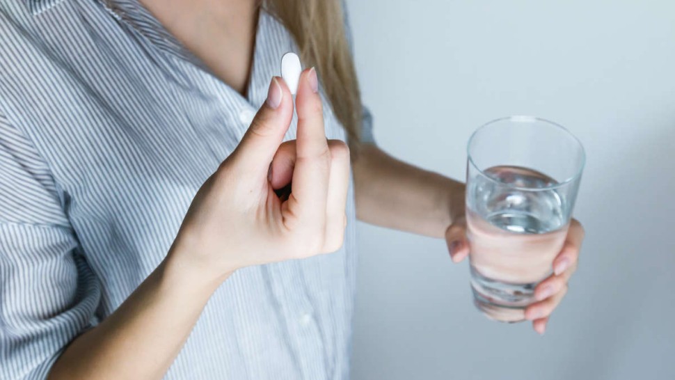 Femme qui consomme un complément alimentaire avec un verre d'eau