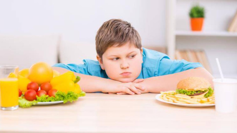 Jeune garçon obèse qui regarde de la nourriture sur une table