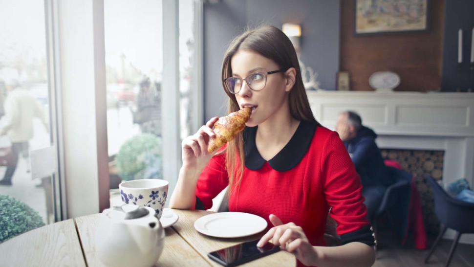 Jeune femme qui mange un croissant dans un café