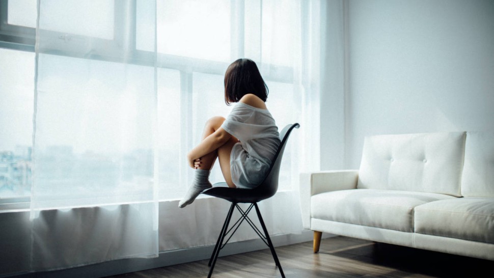 Jeune femme seule devant une baie vitrée