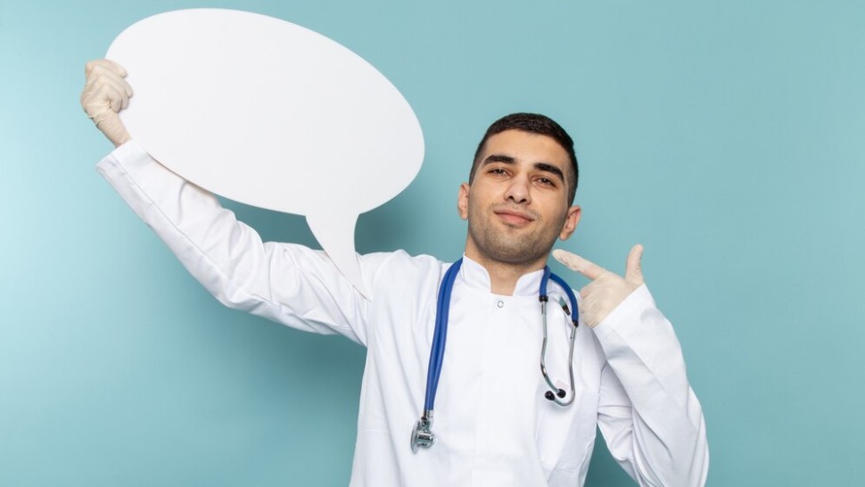 Jeune medecin en costume blanc avec un stethoscope bleu tenant une pancarte blanche