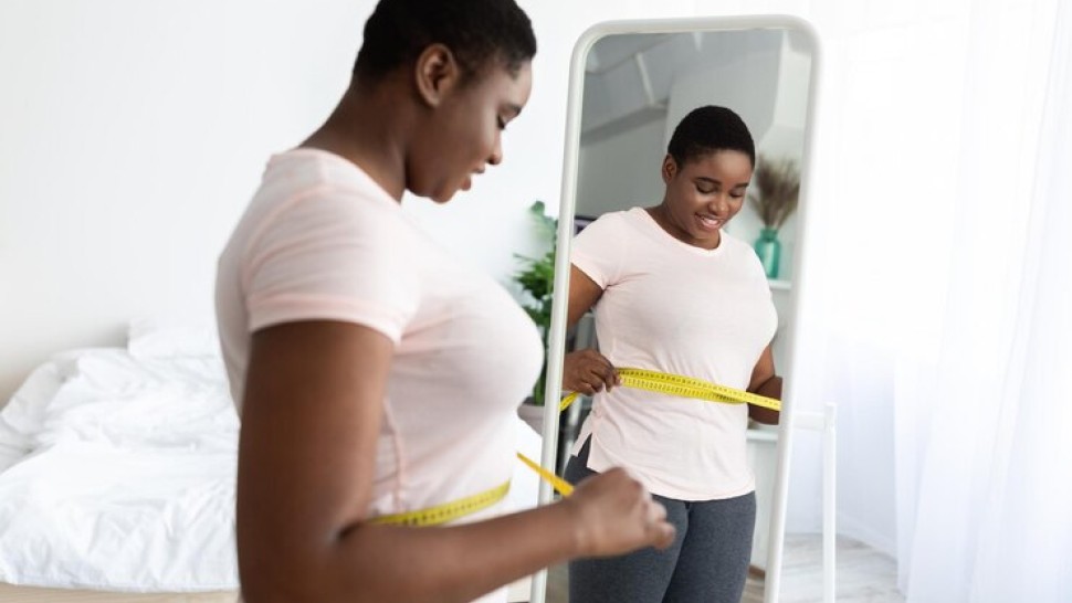 Une femme noire mesurant sa taille avec ruban adhesif debout devant un miroir