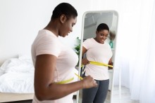 Une femme noire mesurant sa taille avec ruban adhesif debout devant un miroir