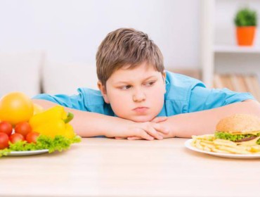 Jeune garçon obèse qui regarde de la nourriture sur une table