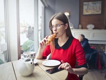 Jeune femme qui mange un croissant dans un café