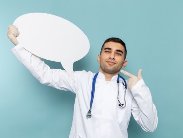 Jeune medecin en costume blanc avec un stethoscope bleu tenant une pancarte blanche