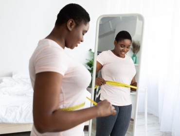 Une femme noire mesurant sa taille avec ruban adhesif debout devant un miroir