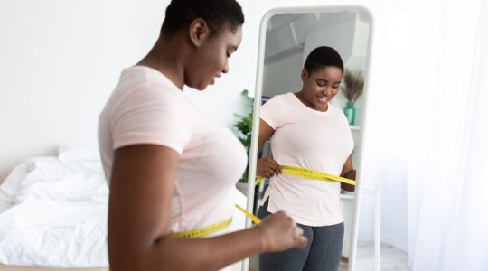Une femme noire mesurant sa taille avec ruban adhesif debout devant un miroir